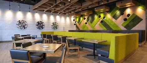 A modern restaurant with wooden tables and benches, a green accent wall, and geometric wall art.
