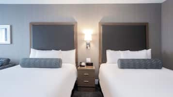 A hotel room with two beds, a nightstand with a lamp, and a small table with a phone and clock.