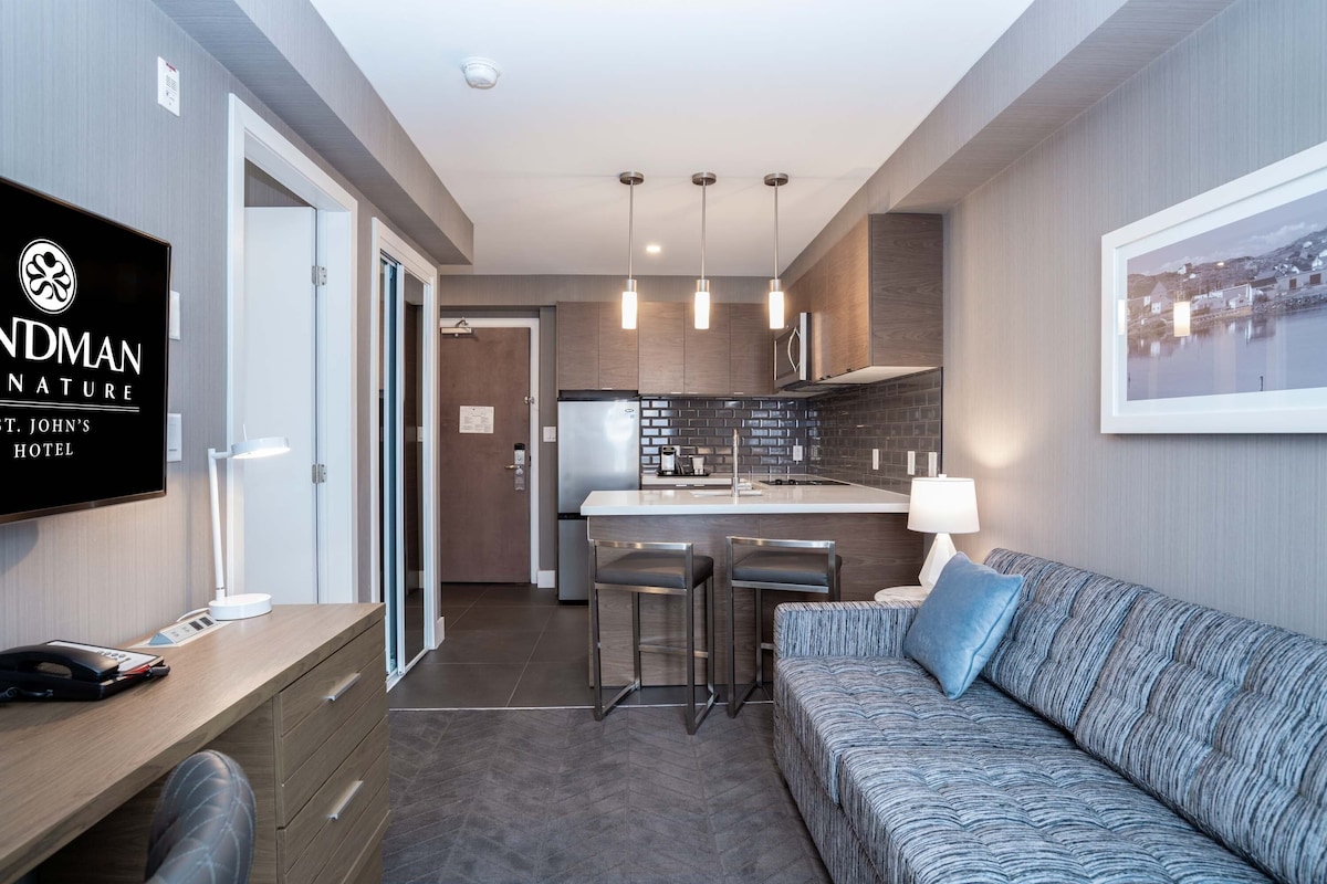 A hotel room with a kitchenette, a sofa, a TV, and a desk with a telephone.