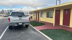 Una camioneta pickup blanca estacionada en un estacionamiento, con un edificio de puertas rojas y fachada amarilla.