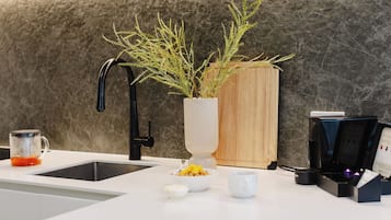 A modern kitchen with a marble backsplash, a coffee machine, a sink, and a potted plant.
