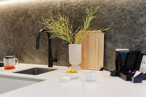 A modern kitchen with a marble backsplash, a coffee machine, a sink, and a potted plant. - Punthill Ivanhoe (Ivanhoe)