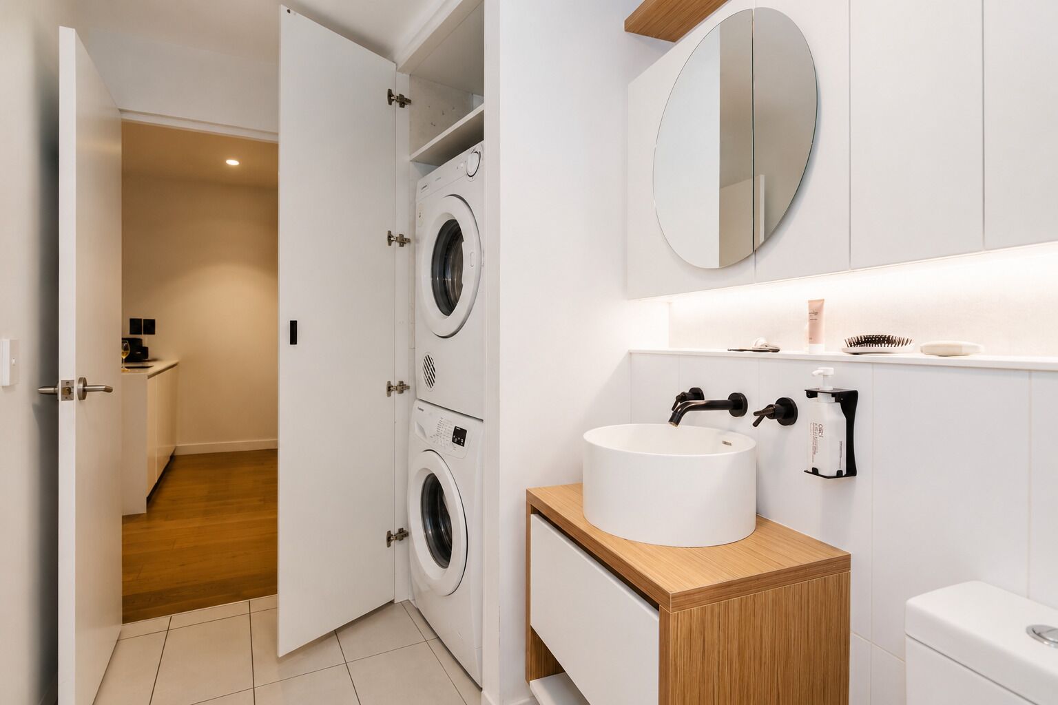 A modern bathroom with a double washing machine, a sink with a mirror above, and a toilet.