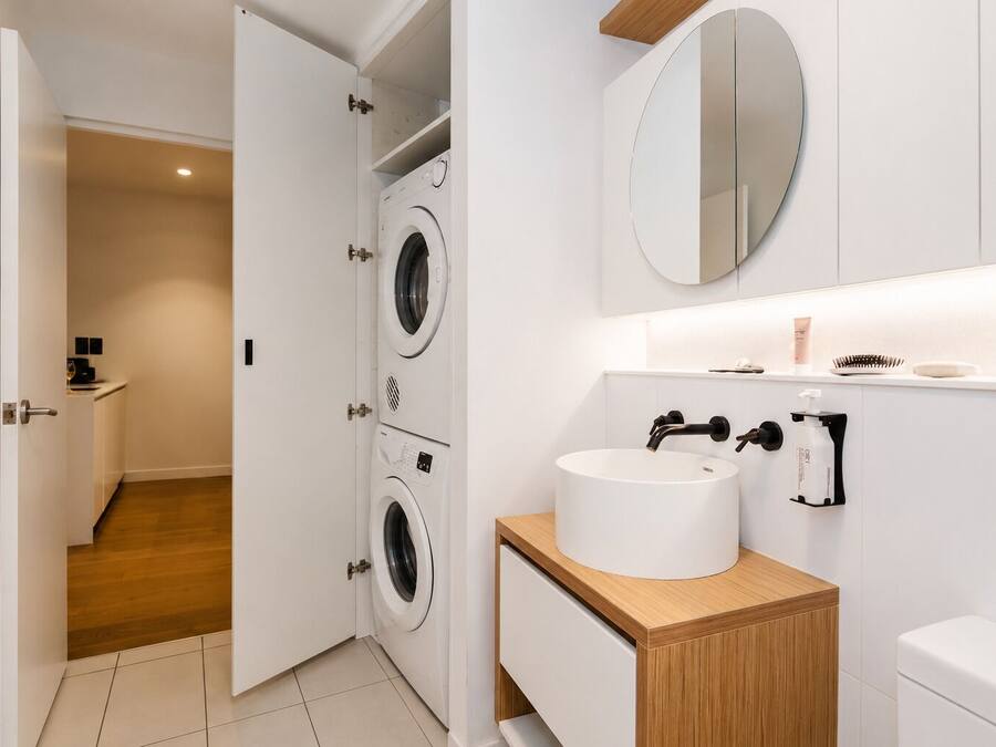 A modern bathroom with a double washing machine, a sink with a mirror above, and a toilet.