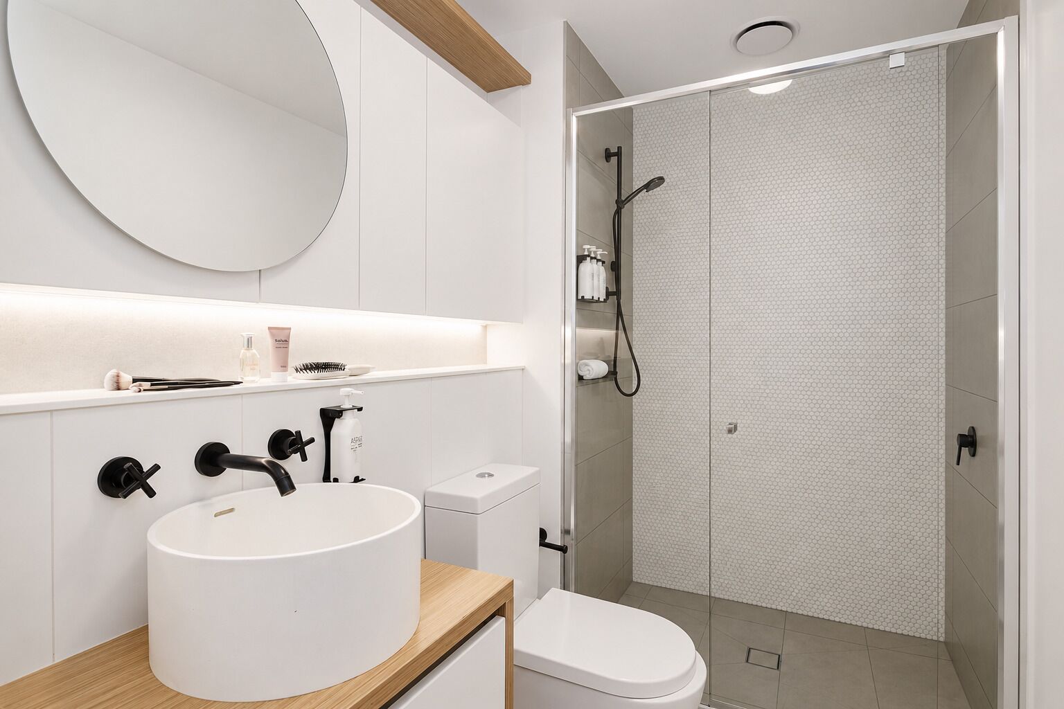 A modern bathroom with a round mirror, a white sink, a toilet, and a shower area.