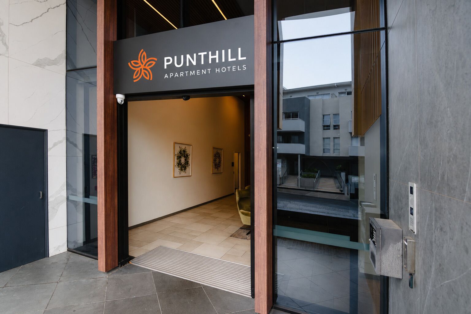 The entrance to Punthill Apartment Hotels with a modern design, including a glass door, a wooden frame, and a sign above the door.