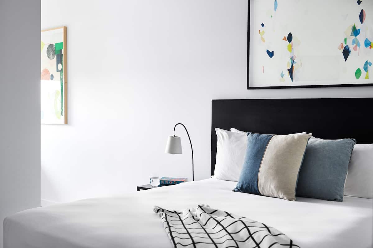 Una habitación de hotel moderna con una cama bien hecha, una mesita de noche con lámpara y arte abstracto en la pared.