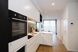 A modern kitchen with a built-in oven, a sink, and a dining area with a window. - Punthill Ivanhoe (Ivanhoe)