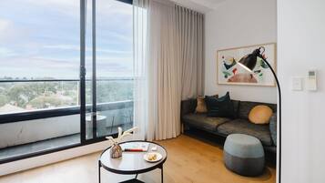 A modern living room with a large window, a sofa, a round table, and a lamp.