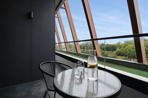 A modern room with a glass table, two chairs, and a view of greenery through large windows. - Punthill Ivanhoe (Ivanhoe)