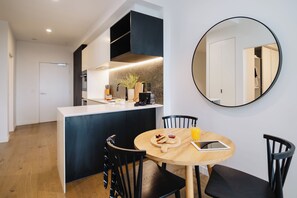 A modern kitchen with a central island, a dining table with chairs, and a round mirror on the wall. - Punthill Ivanhoe (Ivanhoe)