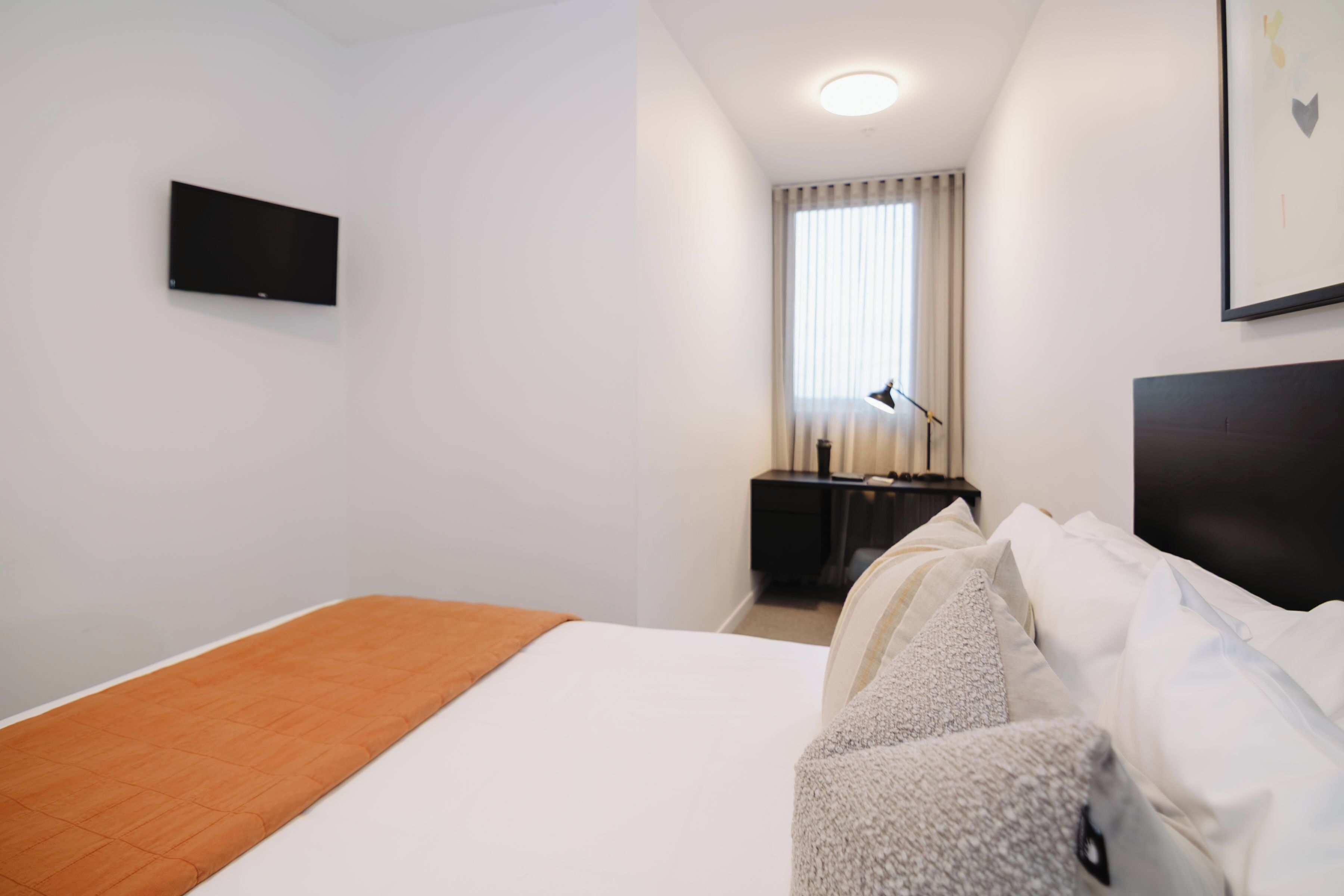 Ett hotellrum med en säng, ett skrivbord, en stol, en tv och ett fönster med gardiner.