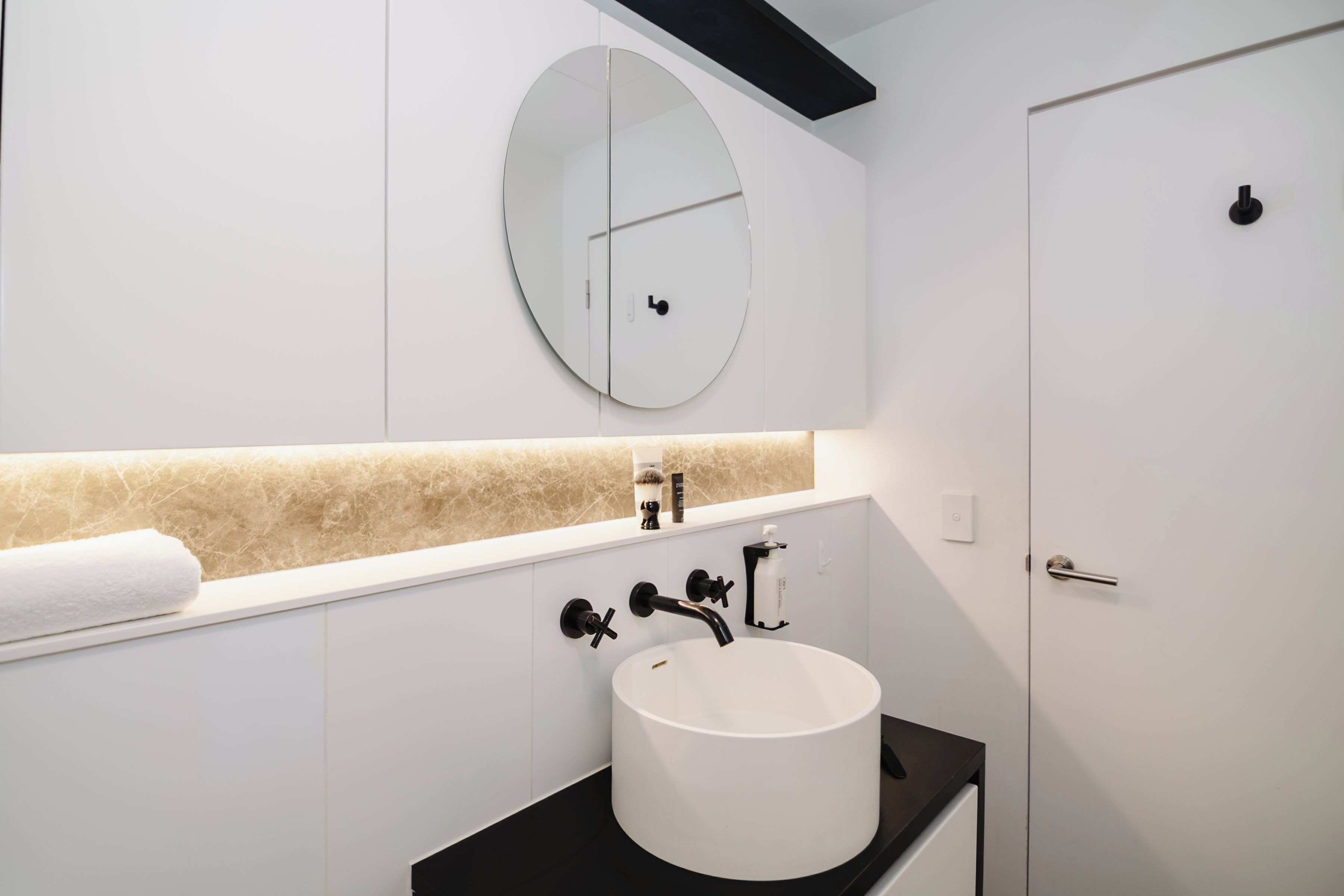 A modern bathroom with a white sink, a round mirror, and a towel on the counter.