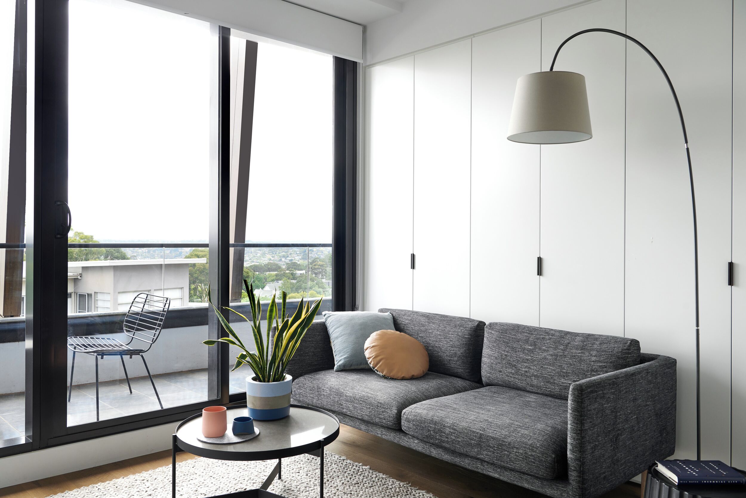 Ein modernes Wohnzimmer mit grauem Sofa, rundem Couchtisch, Zimmerpflanze und Stehlampe.