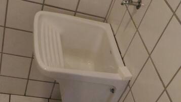 A small, white, square-shaped urinal with a metal handle, mounted on a tiled wall.