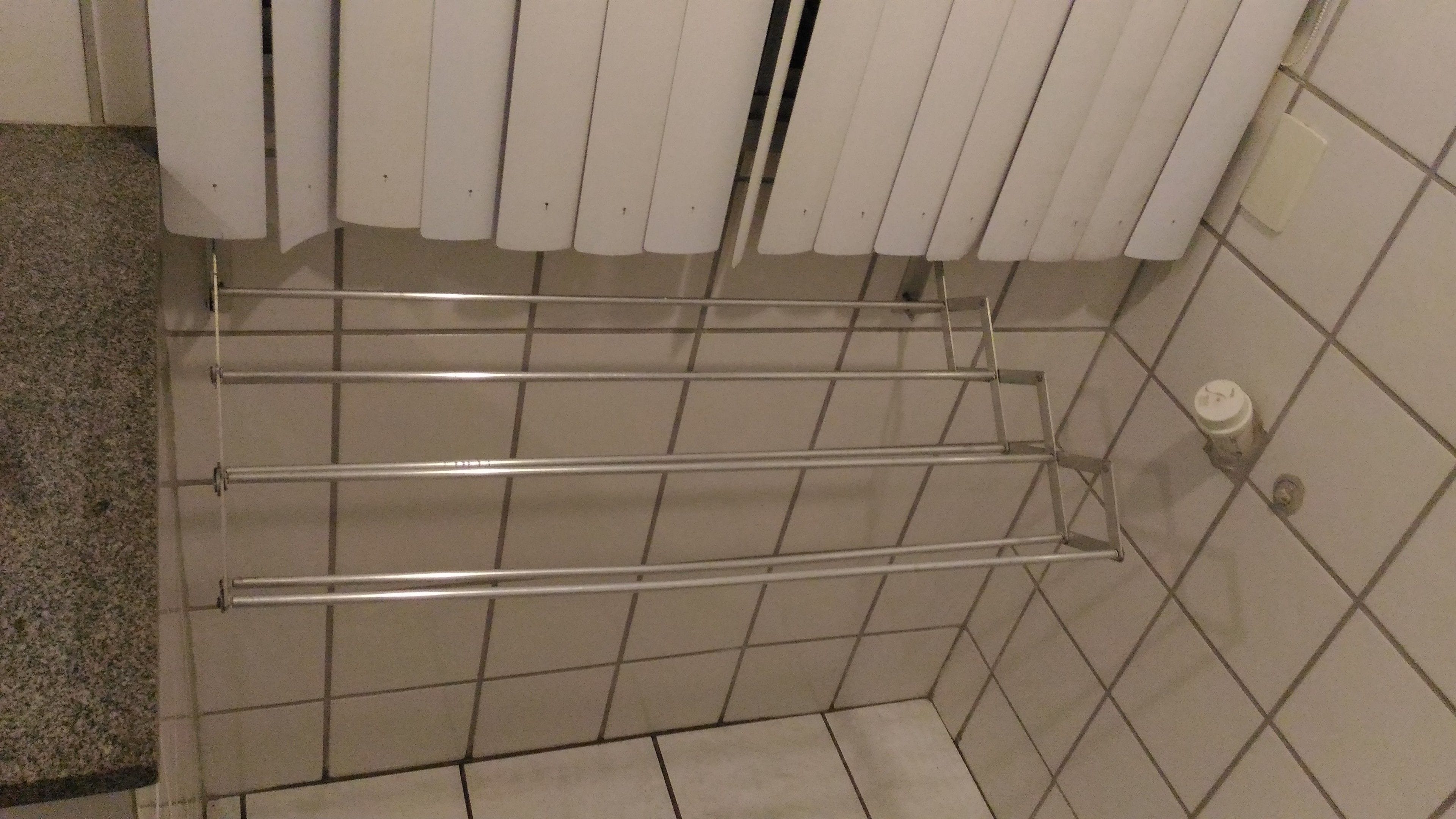 Un baño con baldosas, un perchero metálico, un dispensador de papel higiénico y una esquina con encimera de granito.