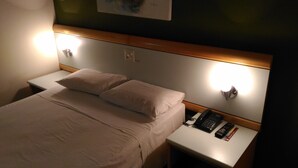 Una habitación de hotel con cama, lámparas de noche, teléfono y control remoto en la mesita de noche.
