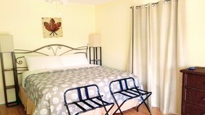 Ein Schlafzimmer mit einem Bett, zwei Stühlen, einem Schminktisch, einem Deckenventilator, einer Wandlampe und einem Vorhang.