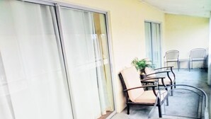 Ein Balkon mit Glastisch und Stühlen, einem Blumentopf und einer Glasschiebetür.