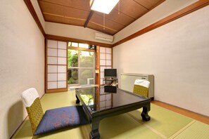 Una tradizionale stanza giapponese con pavimento in tatami, un tavolino, una televisione e una porta scorrevole che dà su un giardino.
