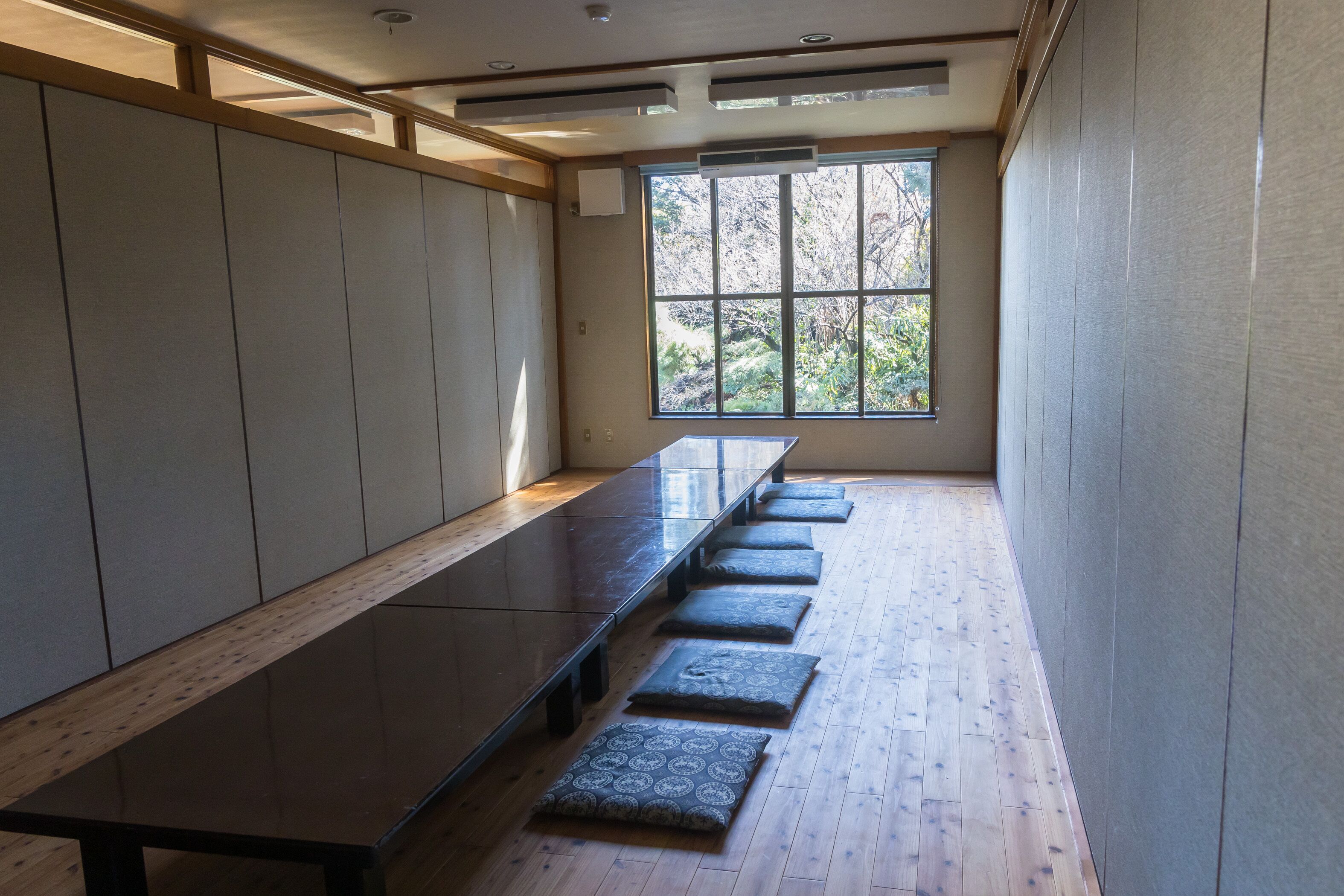 Una larga mesa de madera oscura con una fila de cojines en una habitación con piso de madera y un ventanal grande.