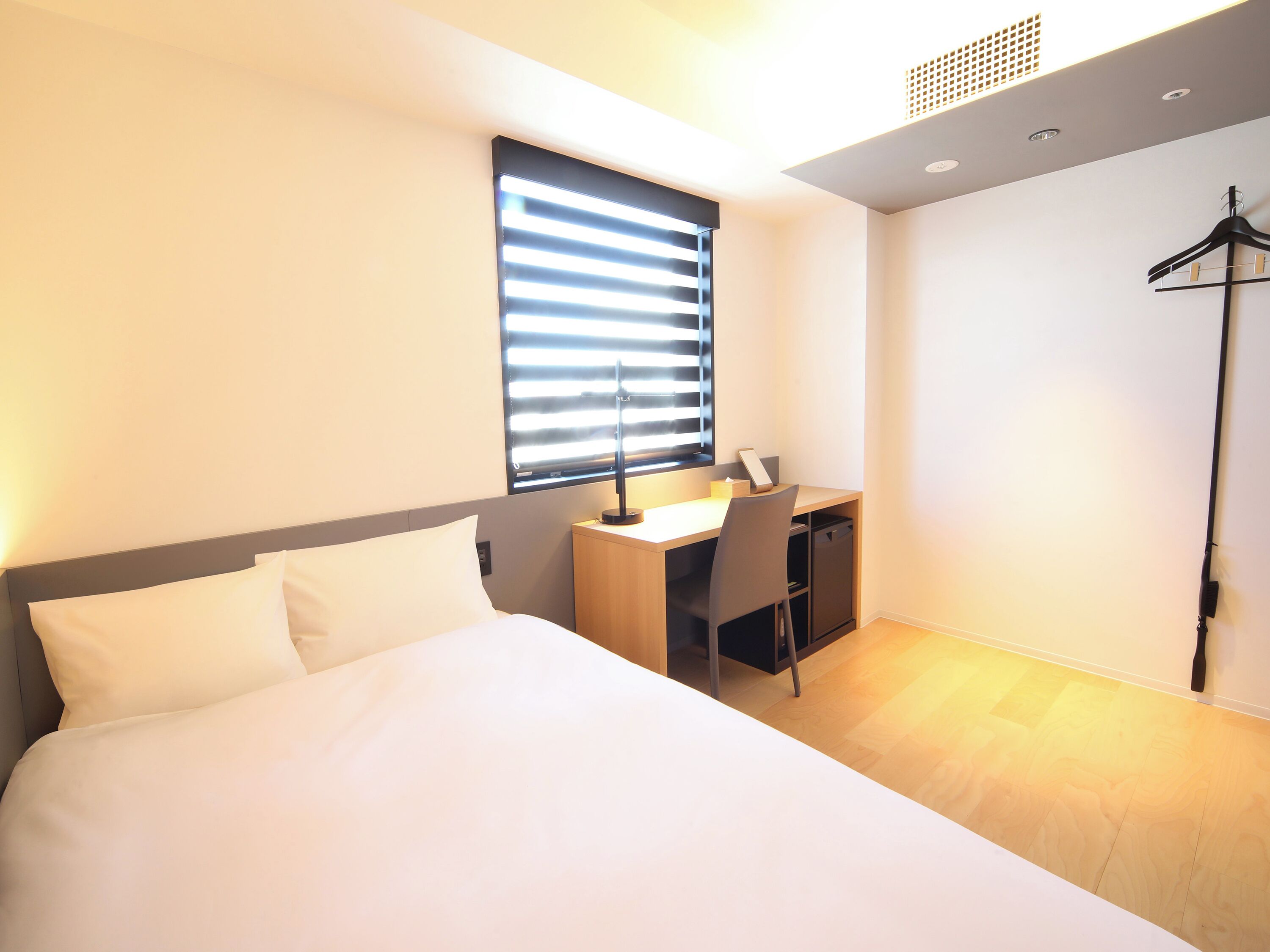 A modern hotel room with a bed, a desk, and a chair.