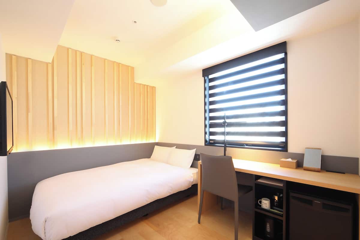 Una habitación de hotel moderna con cama, escritorio, silla y televisión empotrada.