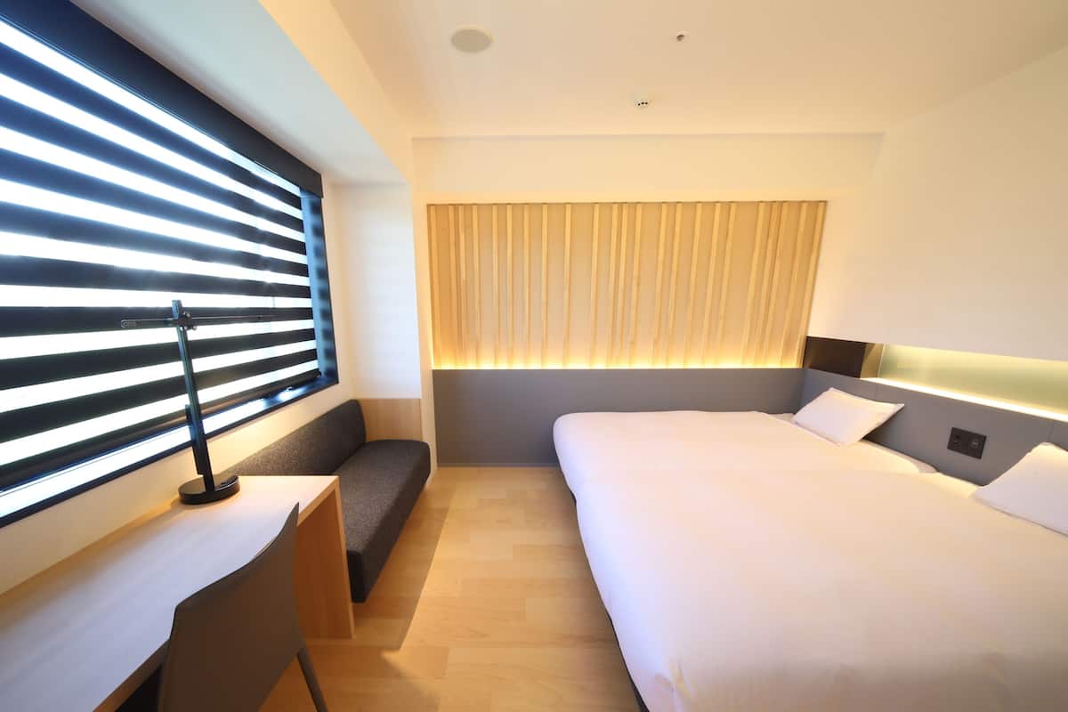 Una habitación de hotel moderna con una cama grande, un escritorio con silla, un banco y una ventana con persianas.