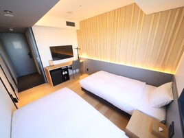 Camera d'albergo con due letti, una scrivania con televisore, un minibar e una porta scorrevole per il bagno.
