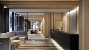 Un área de recepción moderna con un mostrador de madera, un sofá gris y un largo pasillo con paneles de madera y suelo de baldosas.