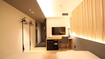 A modern hotel room with two single beds, a desk with a chair, a flat-screen TV, and a wardrobe.