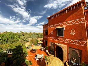 A red building with white geometric patterns, outdoor seating, and a view of greenery.