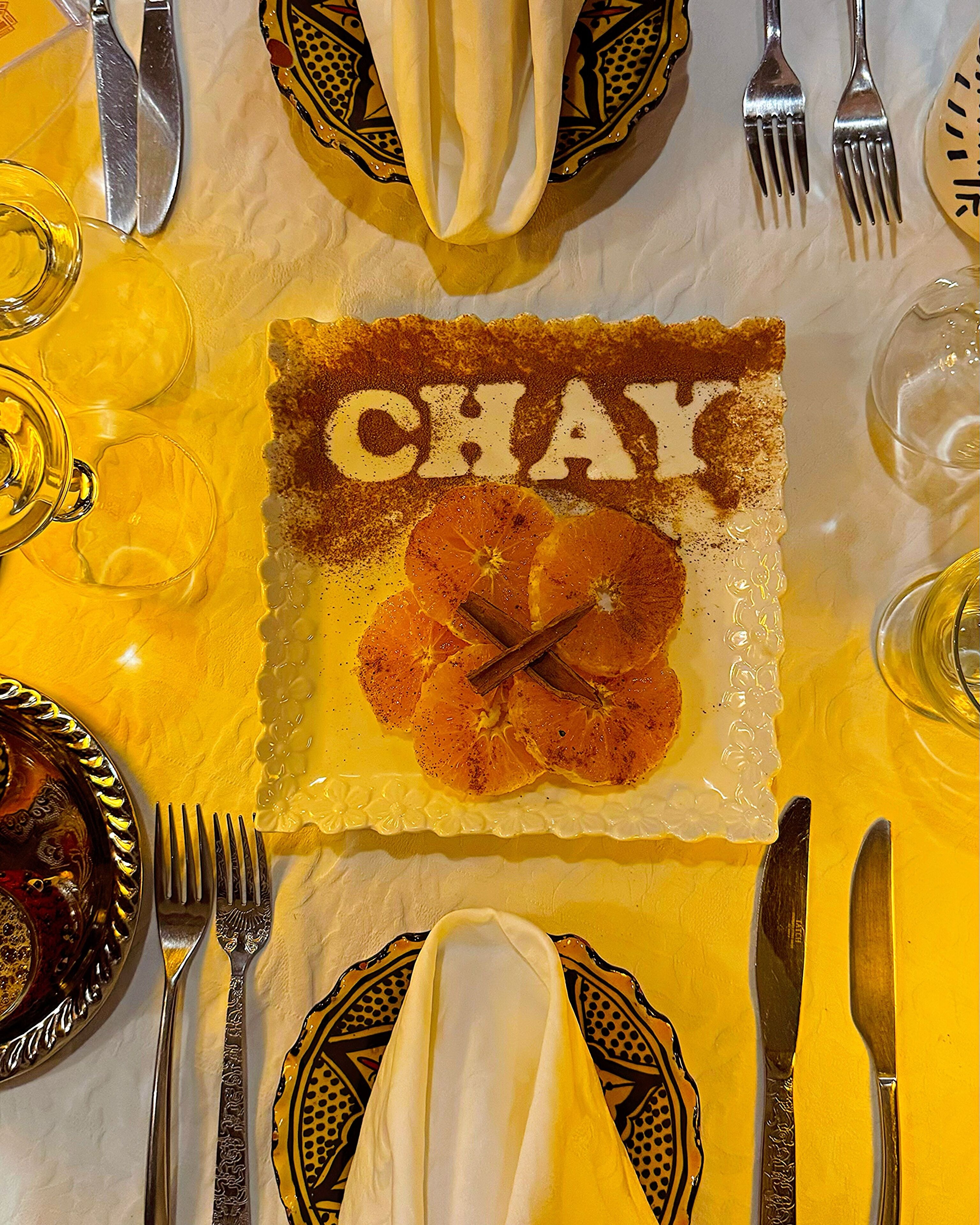 A table set for a meal with a decorative plate featuring the word "CHAY" and orange slices.