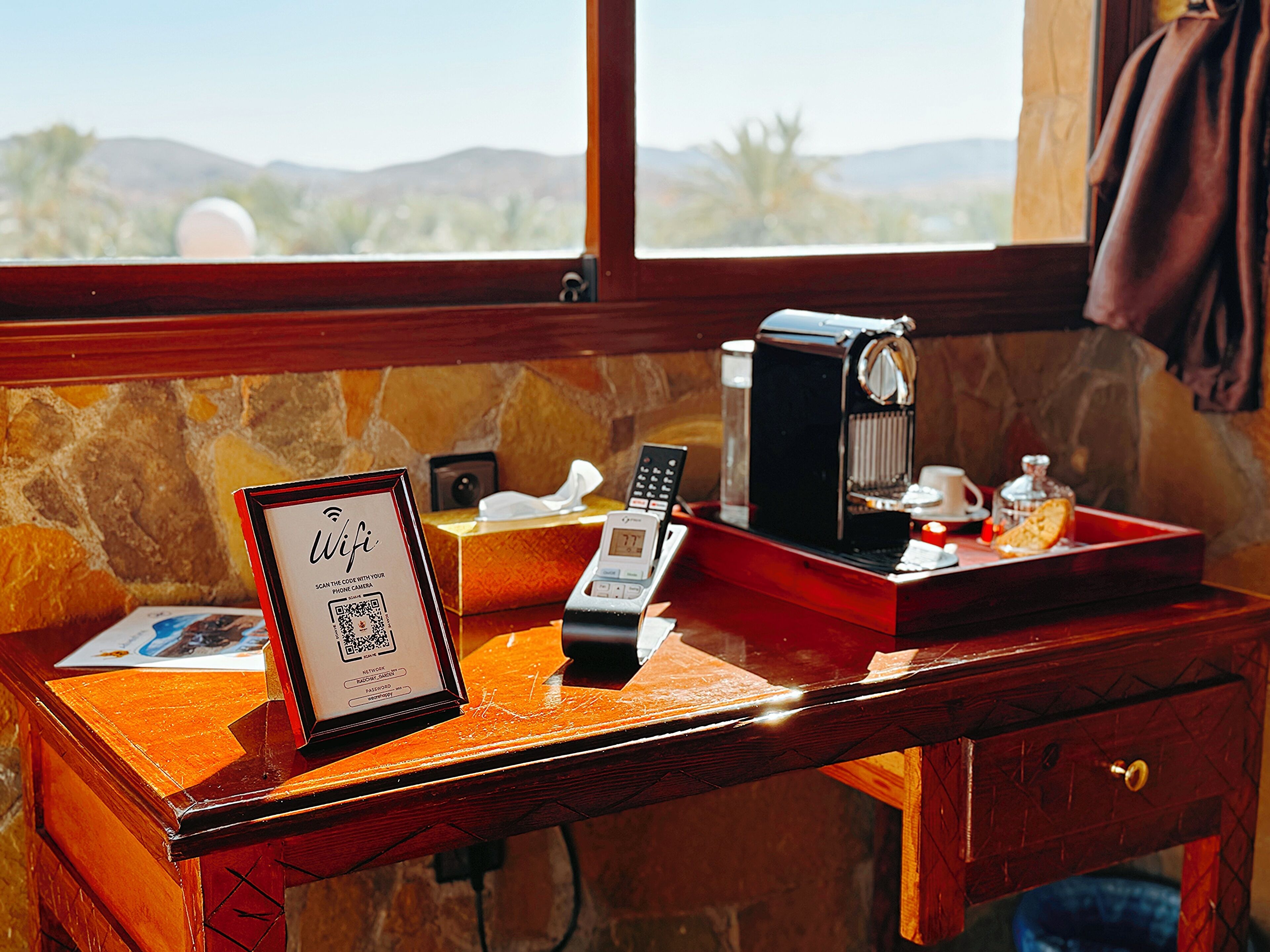 Een houten bureau met een koffieapparaat, een lijst met WiFi-signaal, een zakdoosje en een dienblad met een kop en een fles.