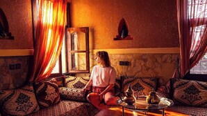 A cozy room with a patterned sofa, a small table with a teapot, and a window with curtains. - Riad Chay & Boutique (Tarmigt)