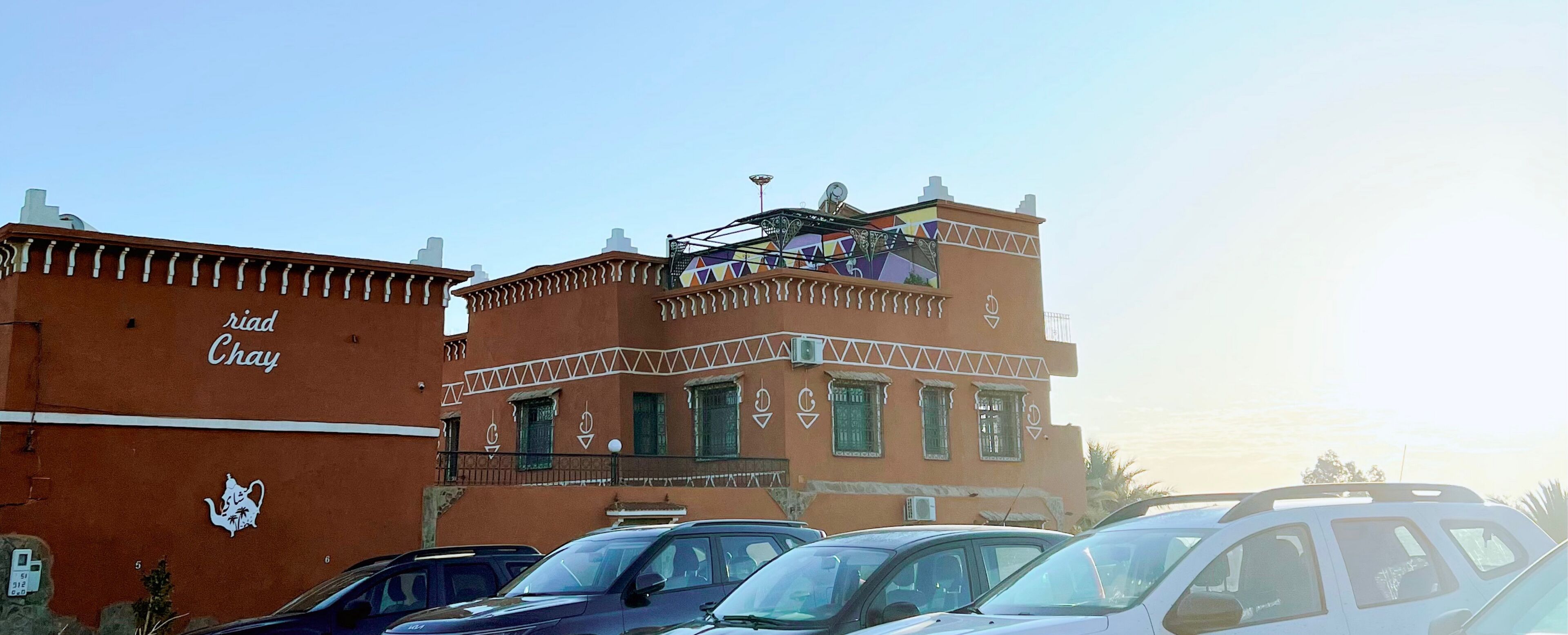 Ein Gebäude mit einem Schild, auf dem "Riad Chay" steht, und einem Wandgemälde an der Fassade.