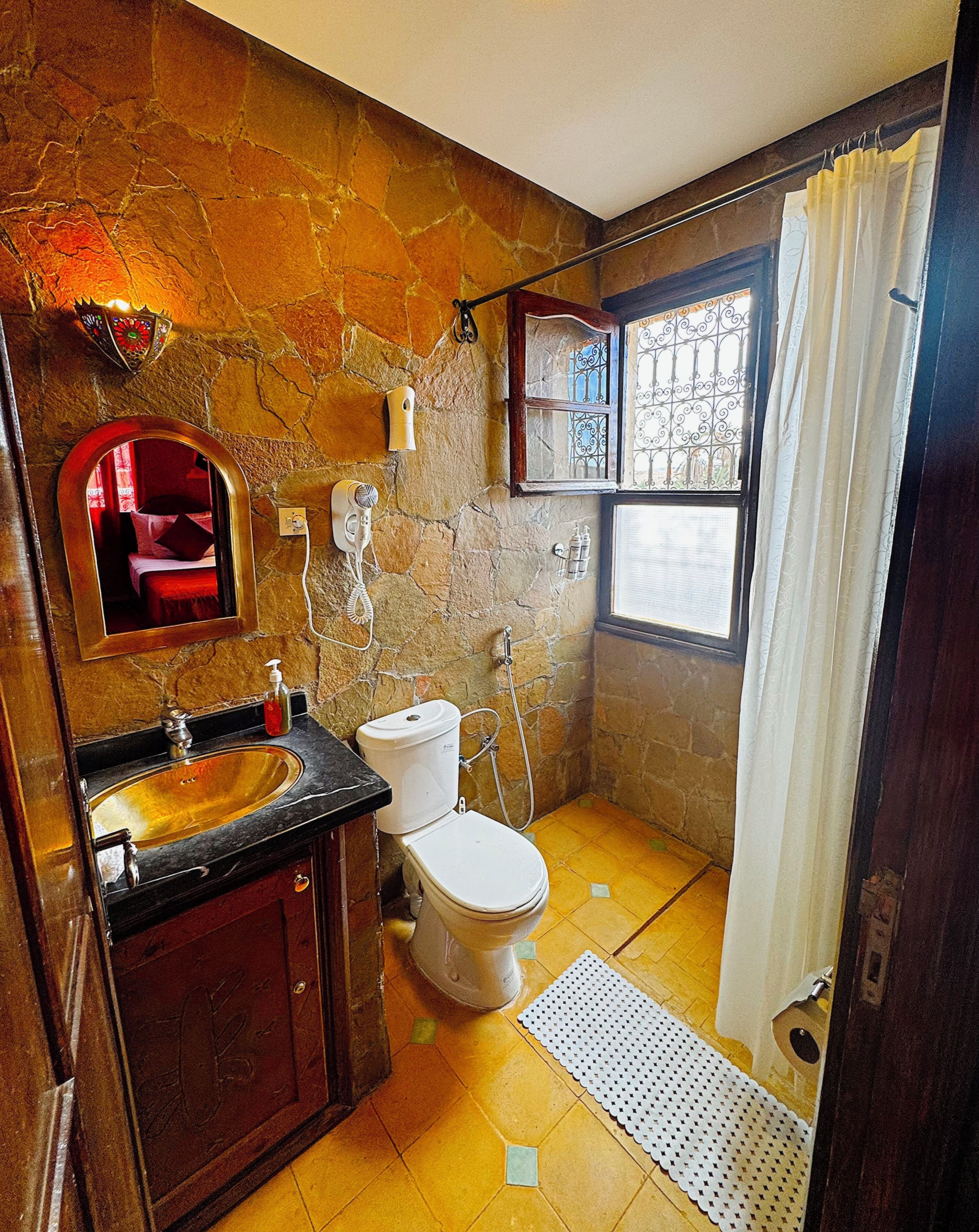 Un baño con pared de piedra, lavamanos, inodoro y zona de ducha.