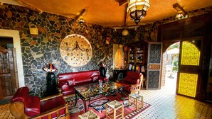 A cozy interior with a stone wall, a red sofa, a wooden coffee table, and a patterned rug. - Riad Chay & Boutique (Tarmigt)