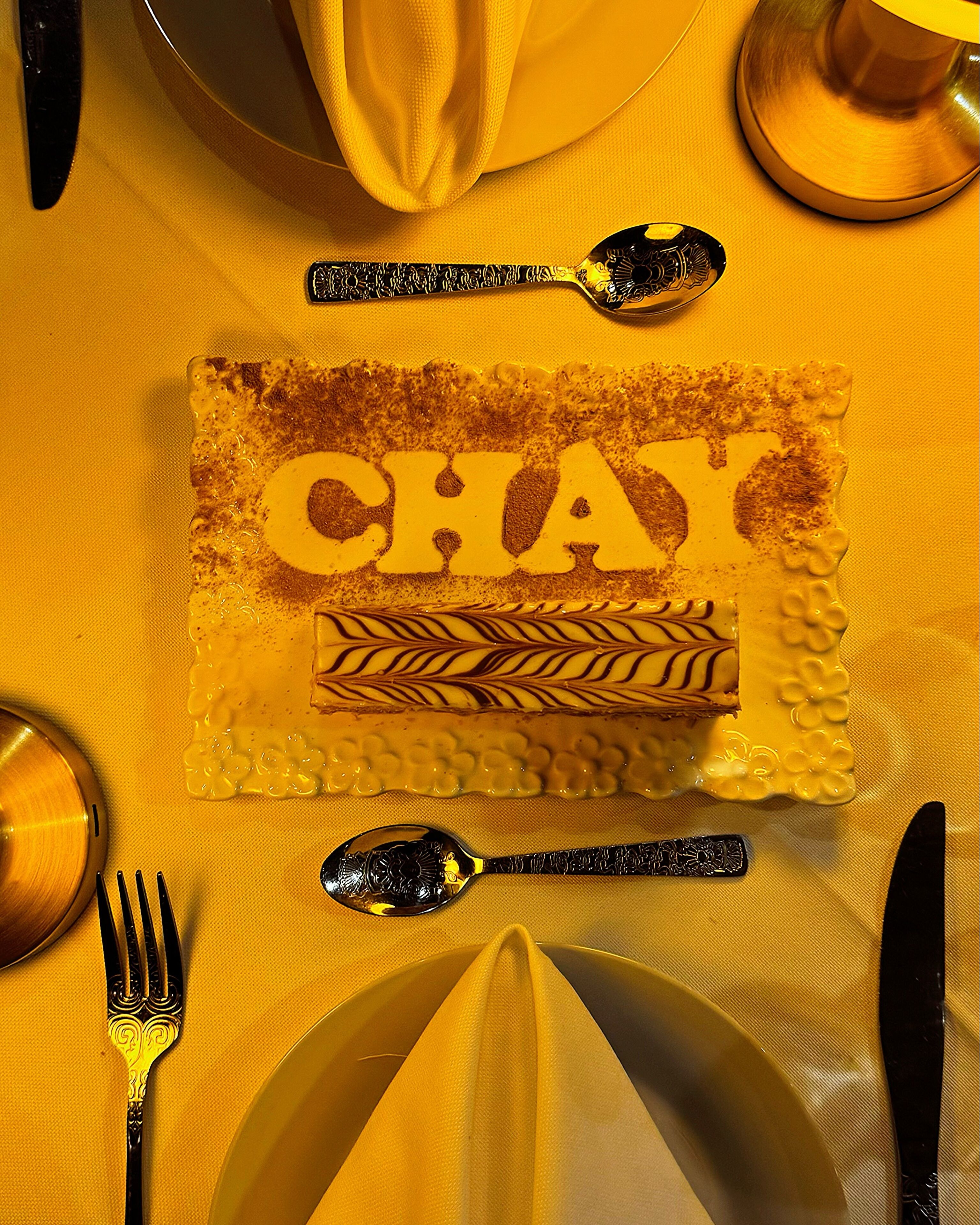 A dessert plate with the word "CHAY" and decorative elements on a yellow tablecloth.