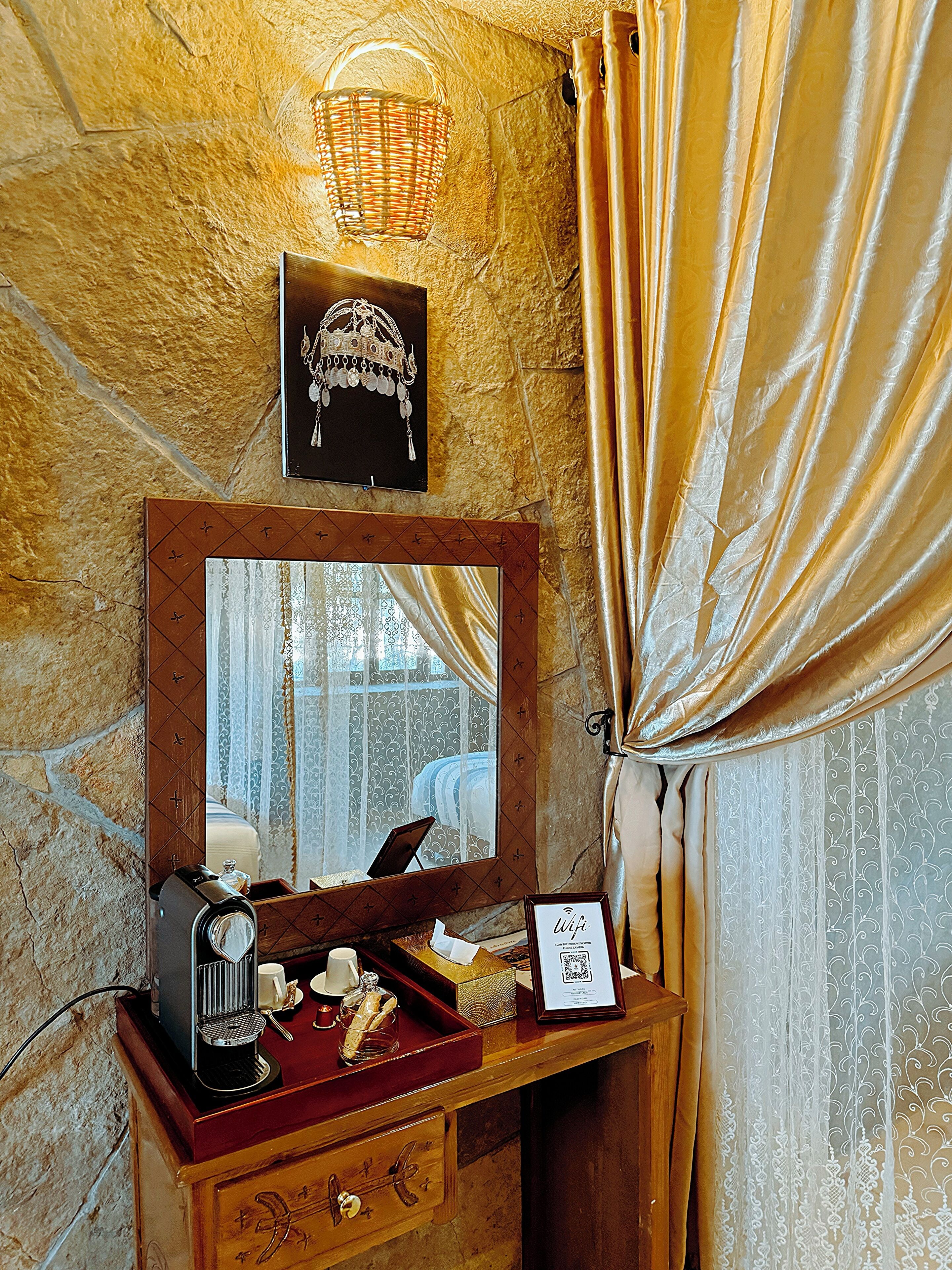 Une coiffeuse en bois avec un miroir, une machine à café et un plateau avec du pain et un verre.