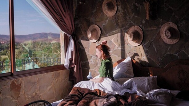 A room with a stone wall, a bed with white and brown bedding, a window with curtains, and a view of the outdoors. - Riad Chay & Boutique (Tarmigt)