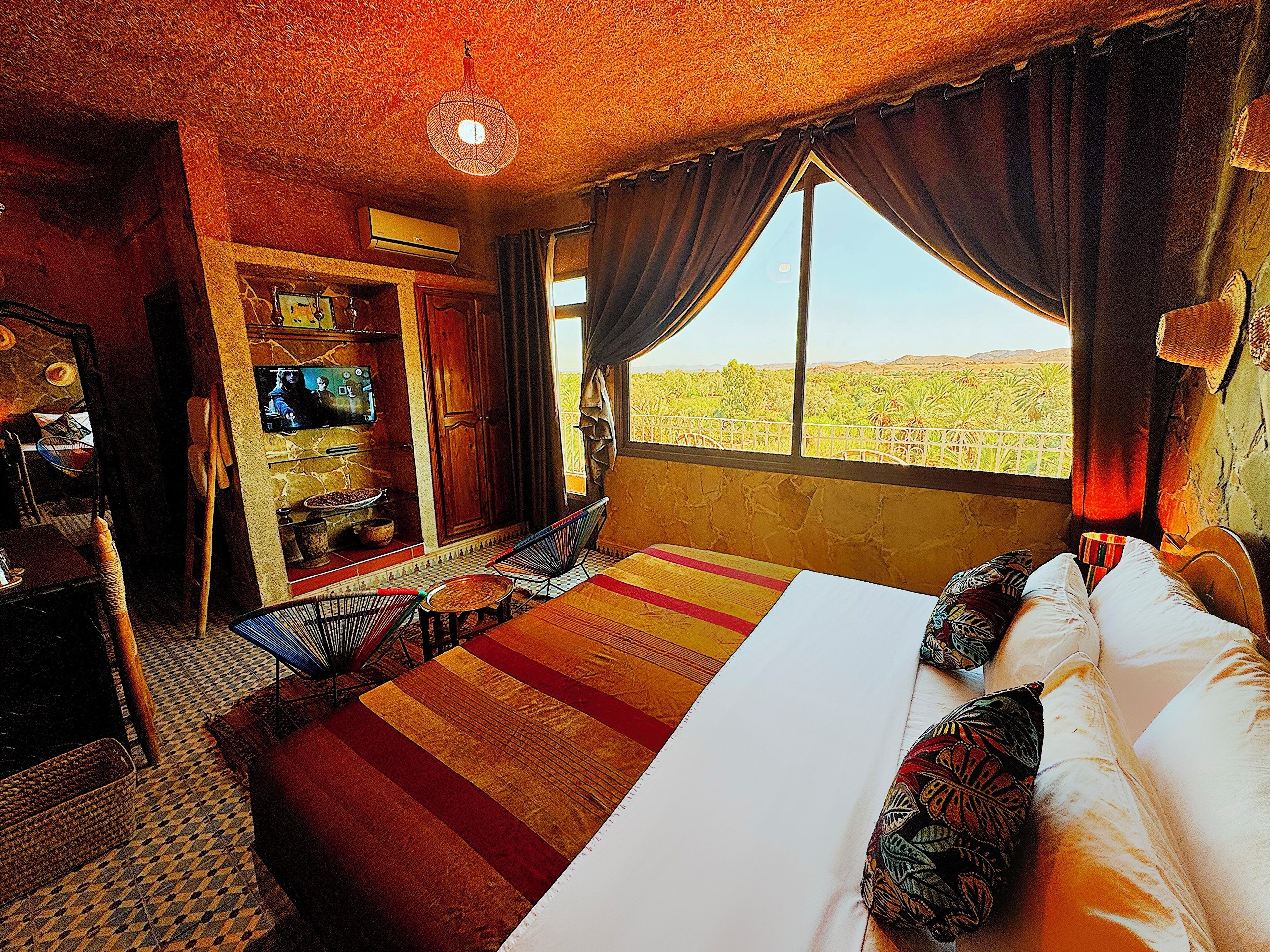 A hotel room with a large bed, a TV, a balcony with a view of the desert, and a patterned carpet.