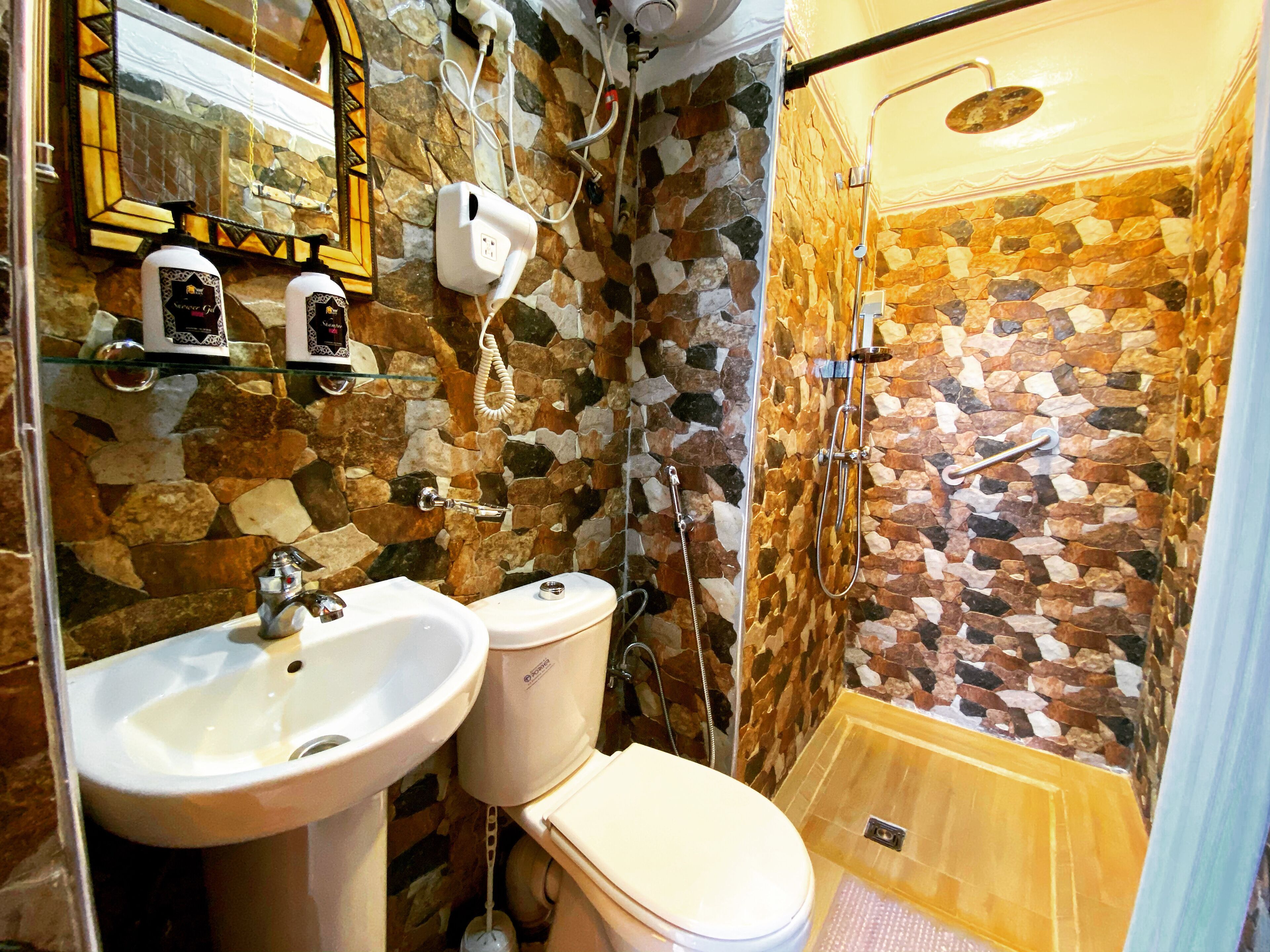 A bathroom with a stone mosaic wall, a glass shower enclosure, and a toilet.