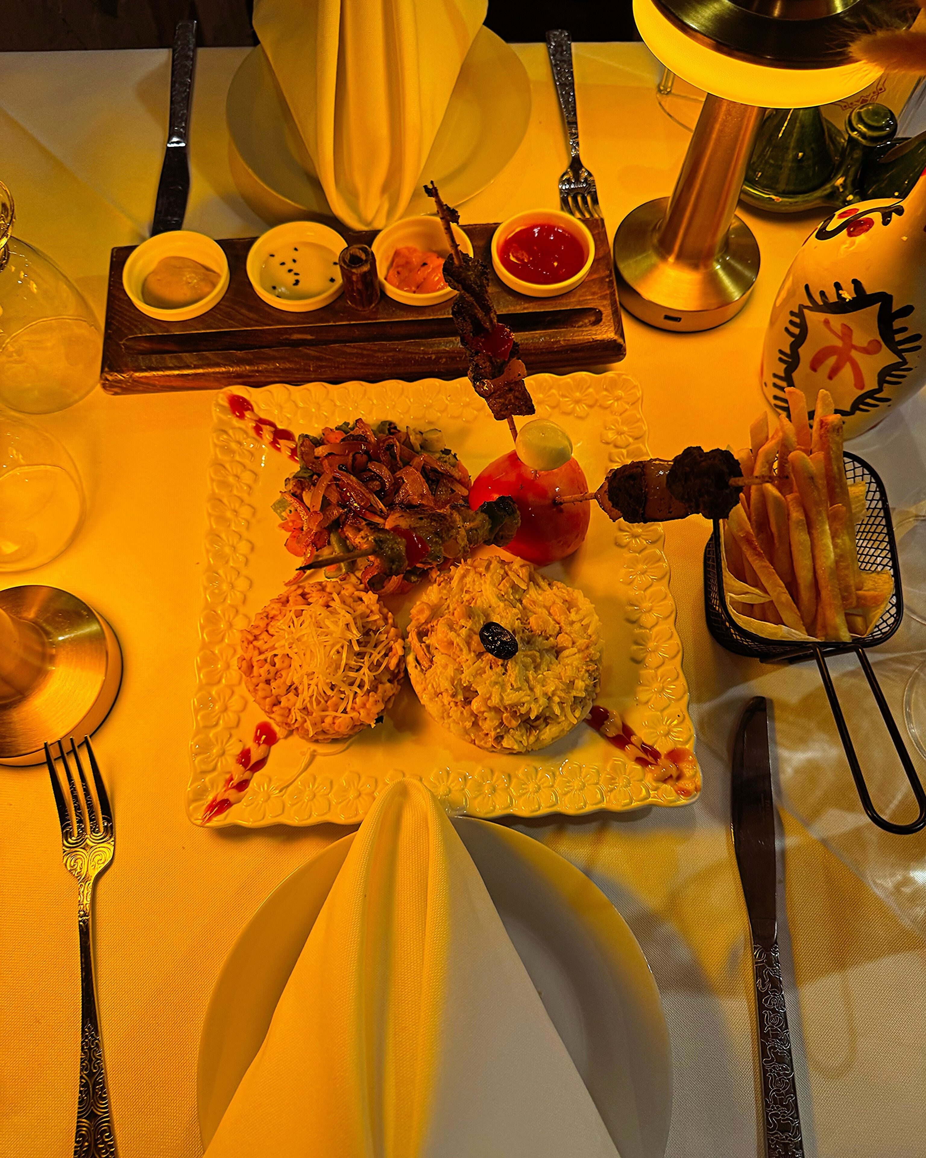 A table set with a variety of dishes including skewers, rice, and a basket of fries.