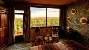 A room with a large window, a bed, two chairs, a small table with fruit, and a decorative wall with hats. - Riad Chay & Boutique (Tarmigt)