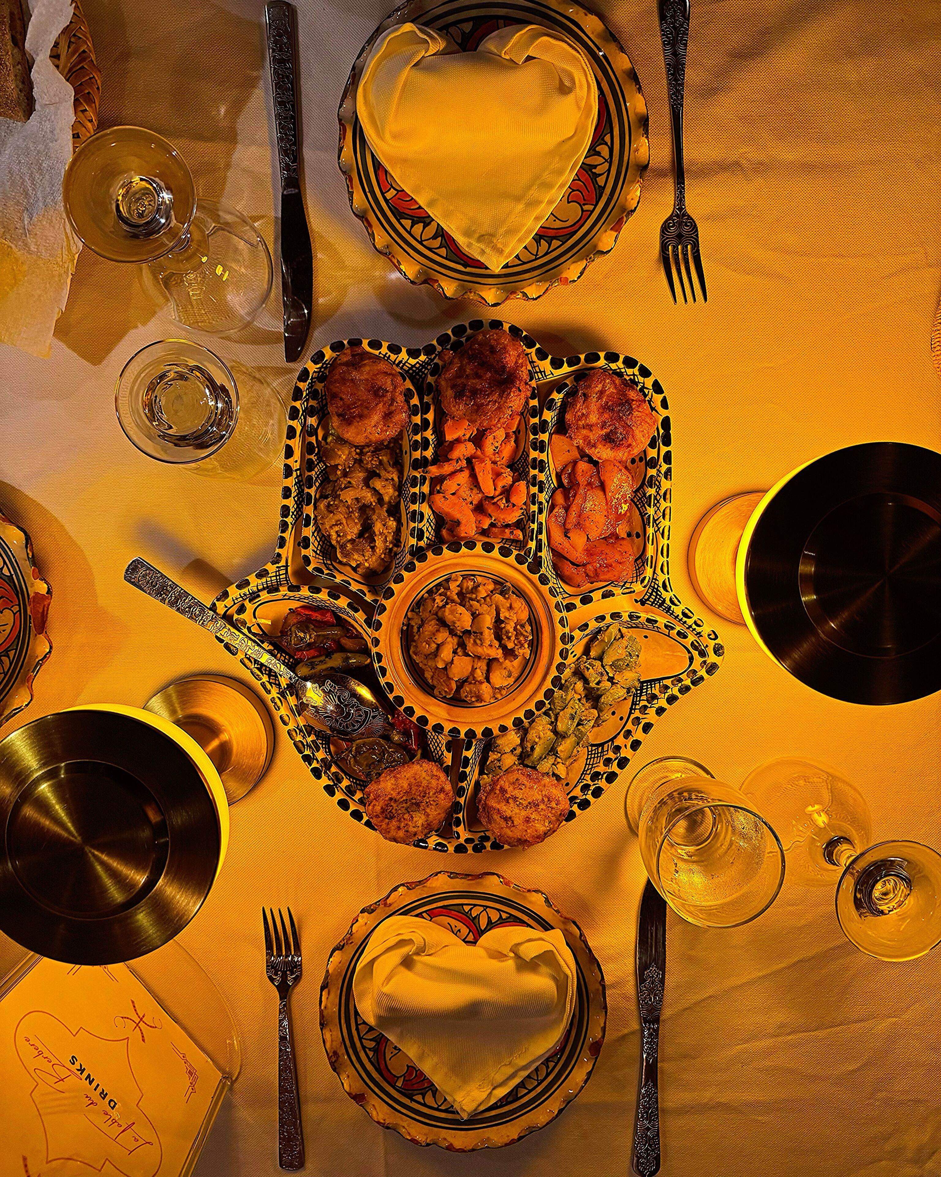 Una mesa servida con diversos platos, que incluyen carne, verduras y pan, junto con copas de vino y cubiertos.