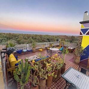 A rooftop terrace with outdoor seating, potted plants, and a view of a lush landscape.
