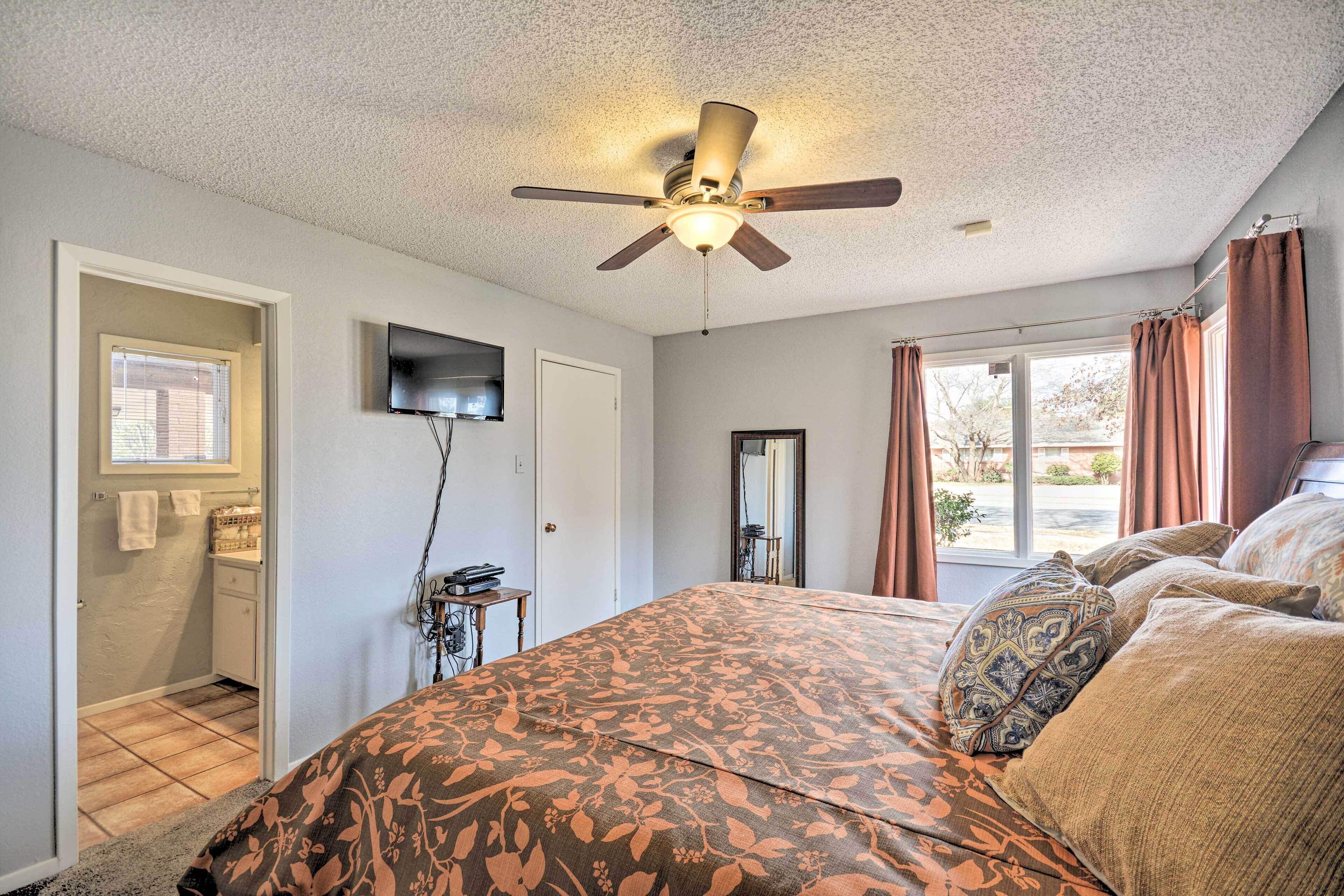 A bedroom with a bed, a ceiling fan, a TV mounted on the wall, and a window with curtains.