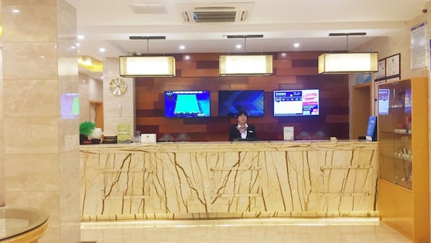 Een hotel receptiebalie met een marmeren aanrecht, twee monitoren en een receptionist.
