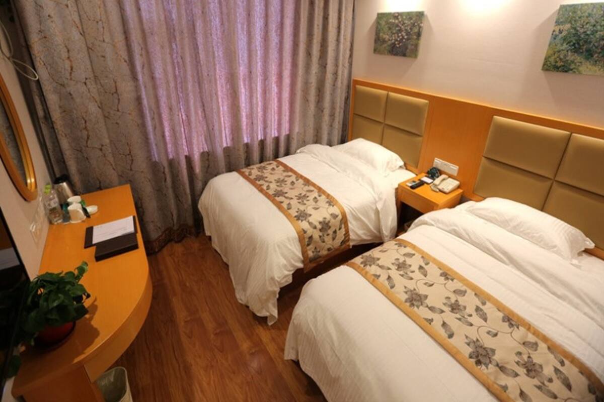 Une chambre d’hôtel avec deux lits, un bureau, un miroir et une plante en pot.